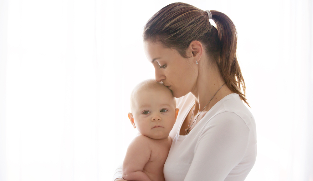 Mother, holding her sick baby boy, sad baby, isolated on white Milwaukee mother with post-partum depression.